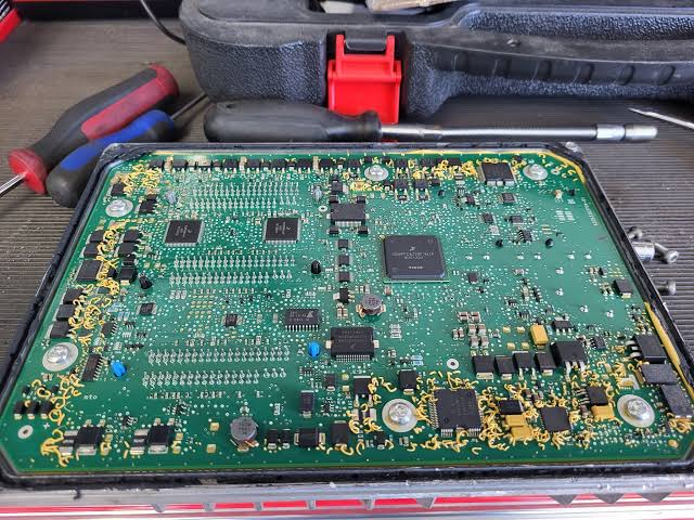 Opened electronic control module on a workbench beside hand tools